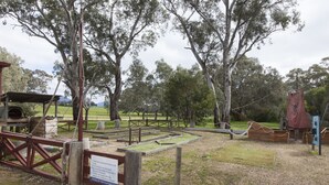 A playground with a swing set, a rope swing, and a fenced play area. - The Apartment (Moyston)