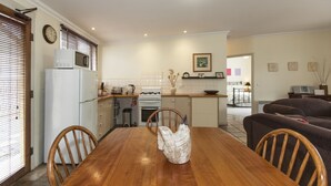 A dining area with a wooden table, chairs, a white refrigerator, a microwave, and a stove. - The Apartment (Moyston)