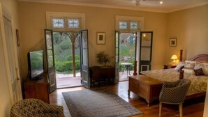 A bedroom with a bed, a chair, a desk, a television, and a view of the outdoors through a door. - Tizzana Winery Bed & Breakfast (Ebenezer)