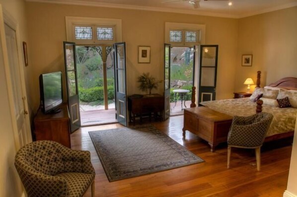 A bedroom with a bed, a chair, a desk, a television, and a view of the outdoors through a door.