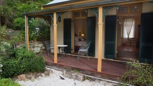 A house with a covered porch, stone walls, and a small table and chair. - Tizzana Winery Bed & Breakfast (Ebenezer)