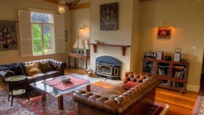 A cozy living room with a fireplace, leather sofas, a coffee table, and a bookshelf. - Tizzana Winery Bed & Breakfast (Ebenezer)