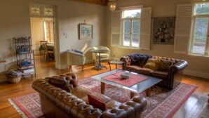 A cozy living room with a leather sofa, a coffee table, and a dining table. There is a window with shutters and a painting on the wall. - Tizzana Winery Bed & Breakfast (Ebenezer)