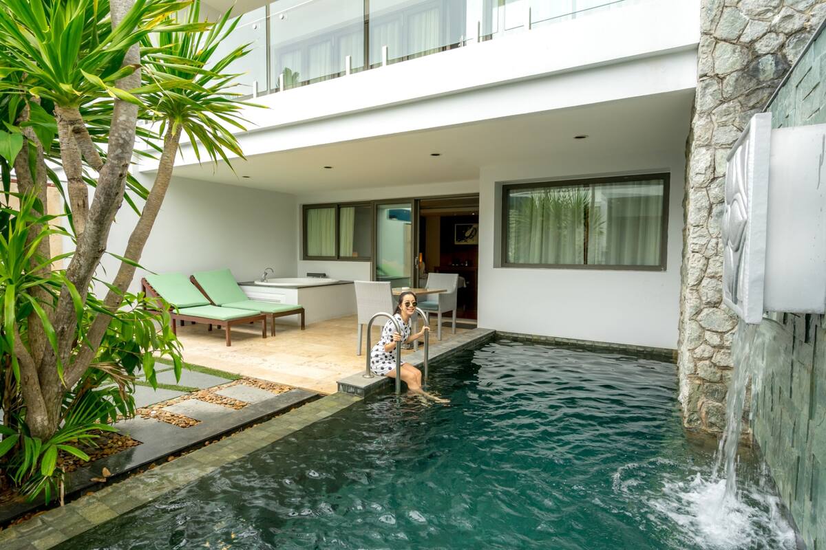 A modern pool area with a stone wall, a lounge chair, and a small waterfall feature.