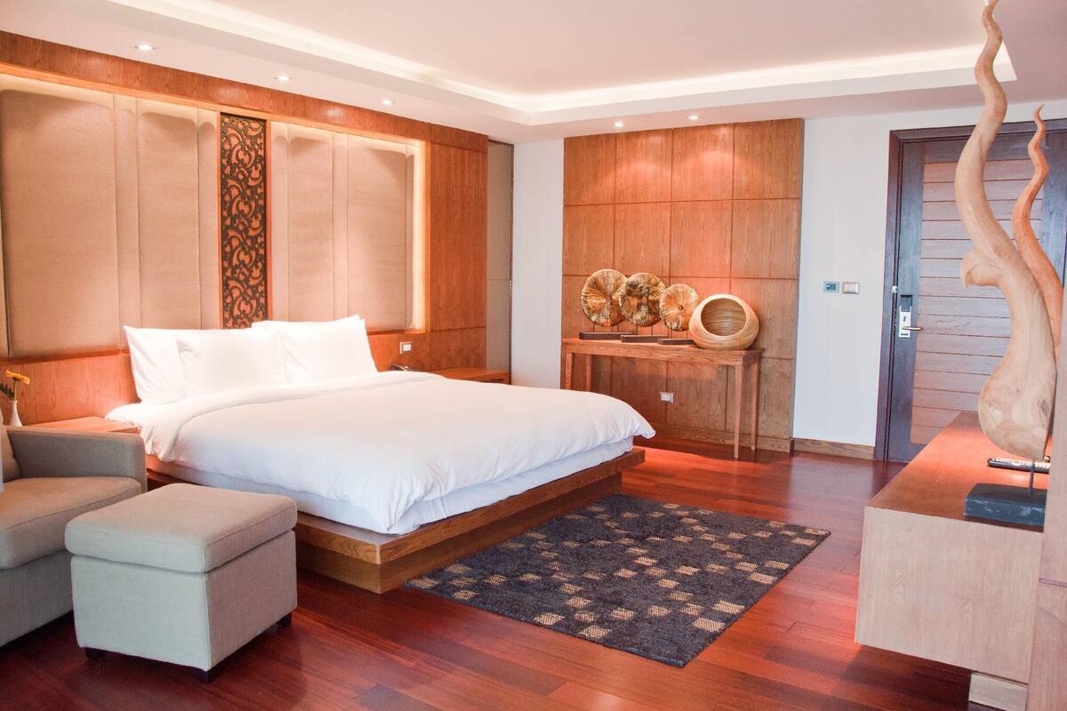 A modern bedroom with a large bed, wooden paneling, a console table with decorative items, and a unique wall sculpture.