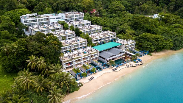A multi-story hotel with a pool and beach access, surrounded by dense tropical vegetation.