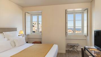 Habitación de hotel con cama, escritorio, televisión y dos ventanas con vista al mar.