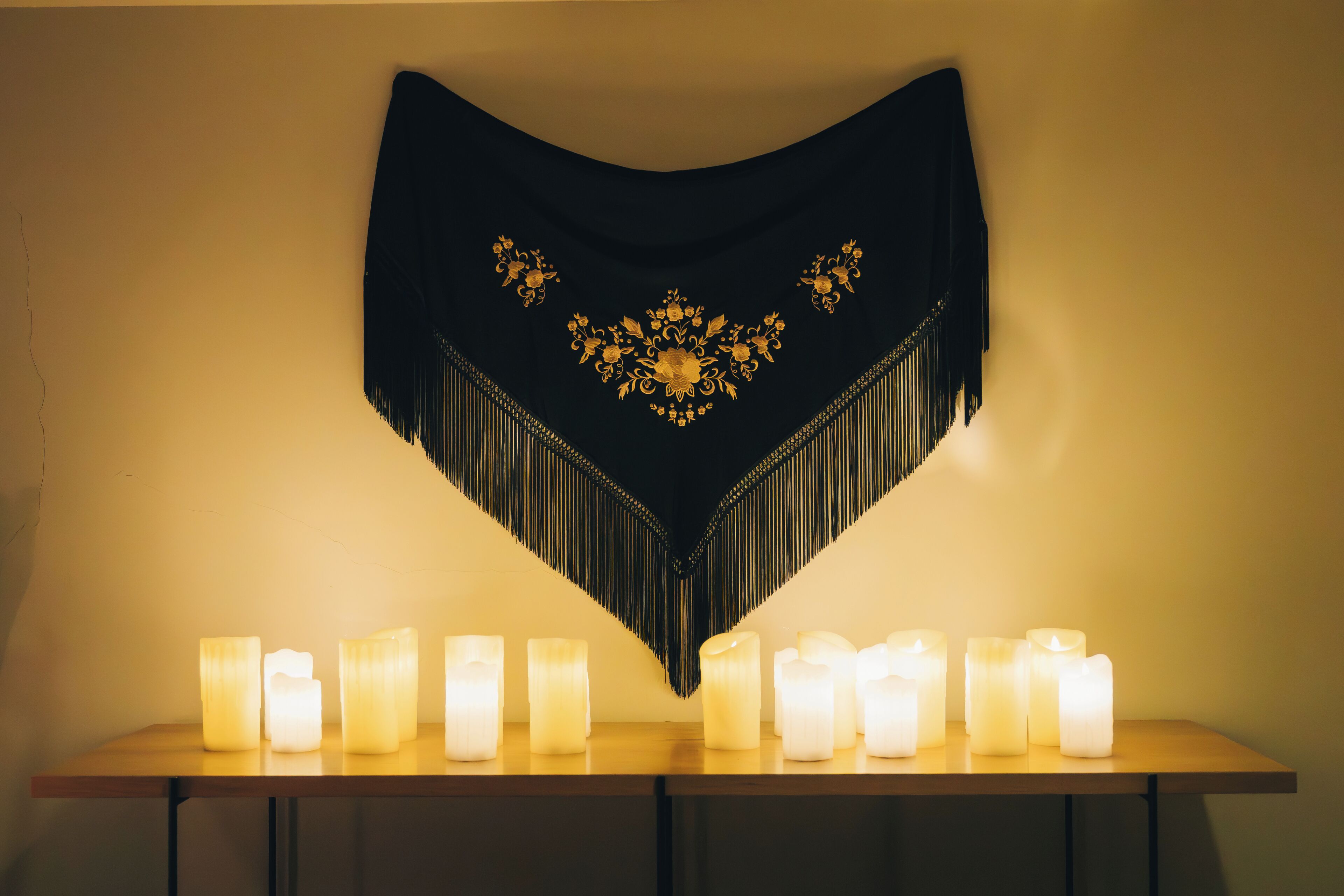 A table with multiple lit candles and a decorative black tapestry with gold embroidery.
