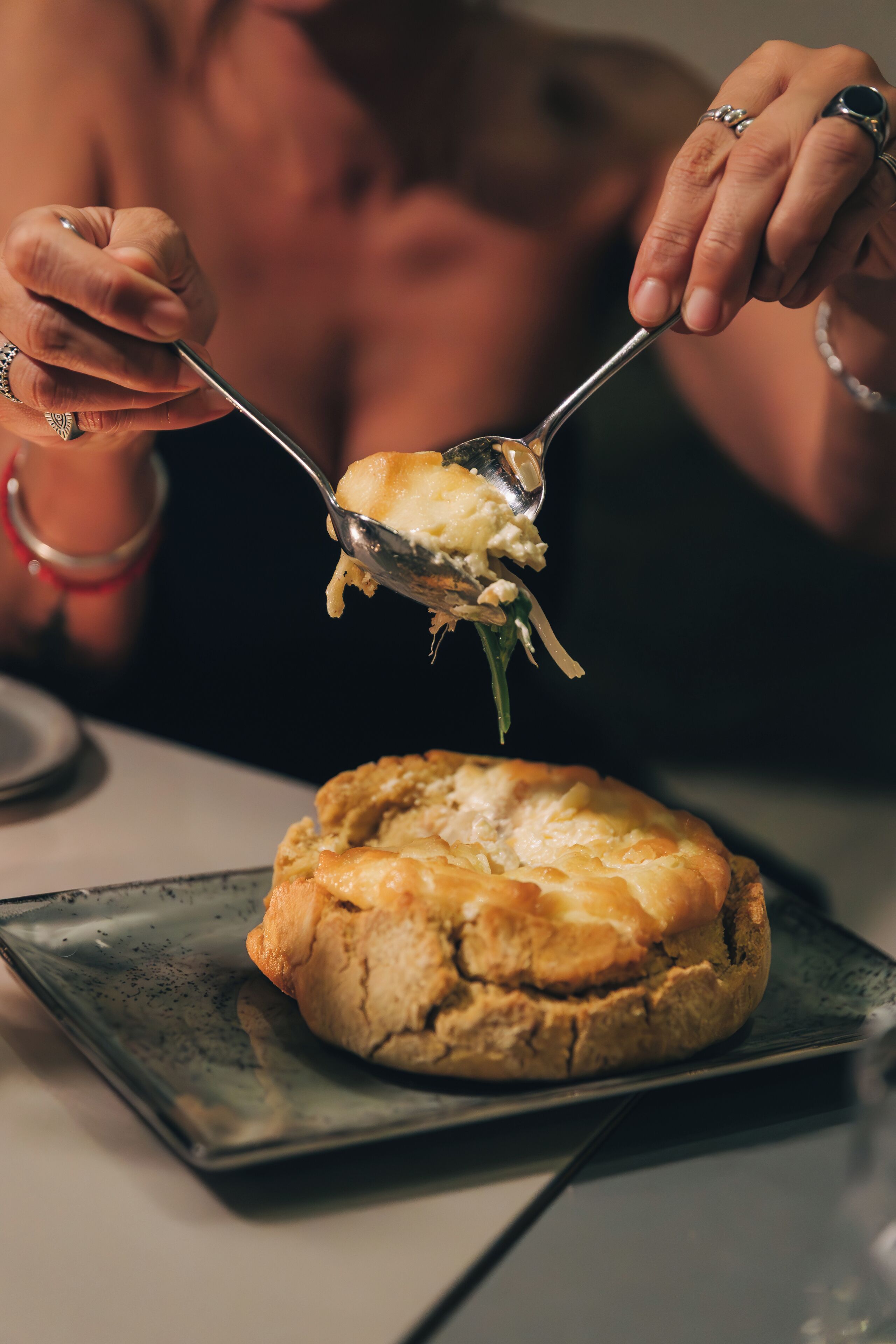 A person using a spoon to serve food from a round, baked dish on a plate.