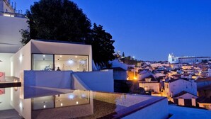 A modern hotel with a glass infinity pool, a terrace, and a view of a historic cityscape at dusk. - Memmo Alfama - Design Hotels (Lisbon)