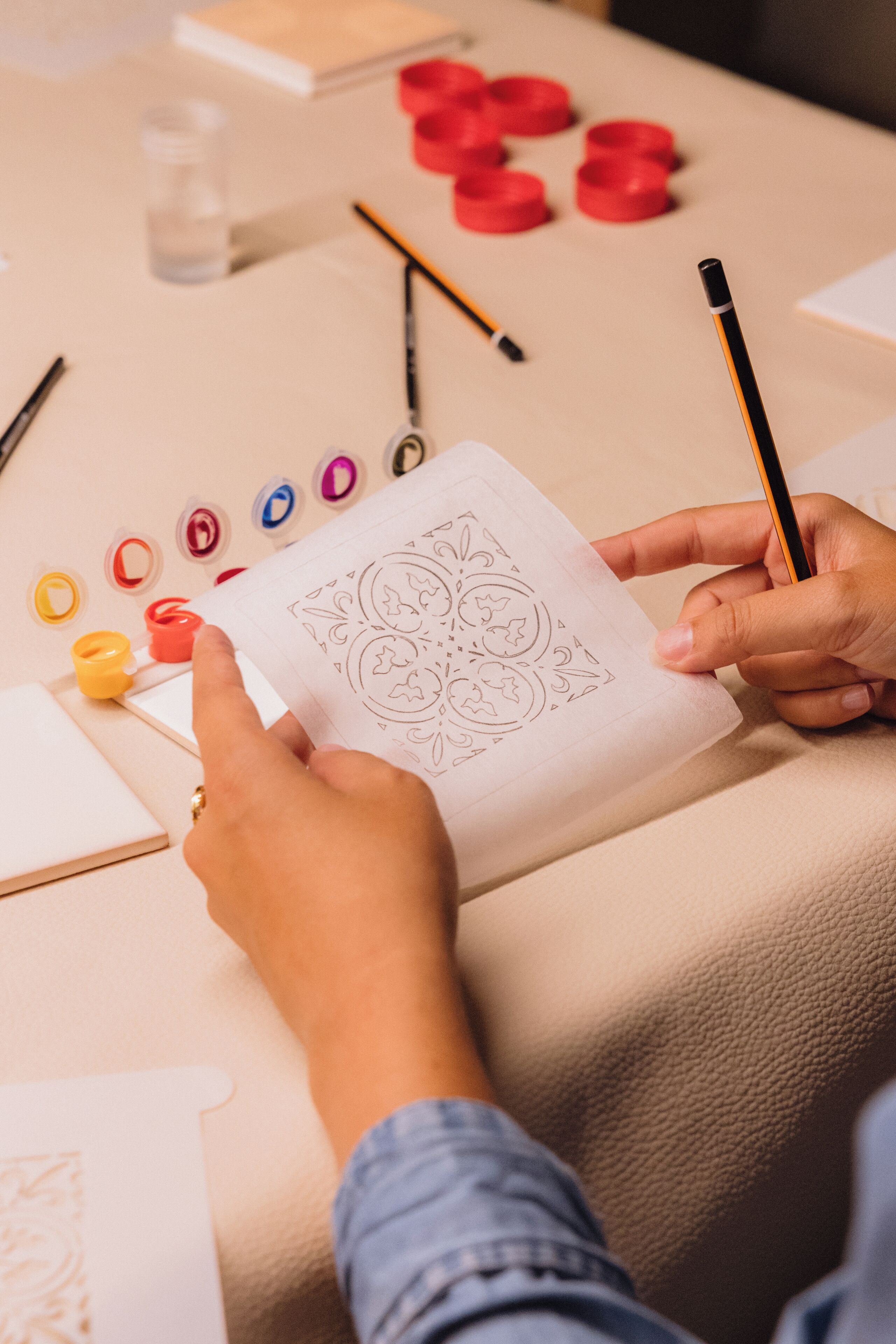 Una persona disegna su un foglio con una matita, circondata da materiali artistici come barattoli di pittura e pennelli.