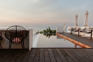 Eine Terrasse mit Holzboden, Stühlen und Sonnenschirmen mit Blick auf ruhiges Wasser.