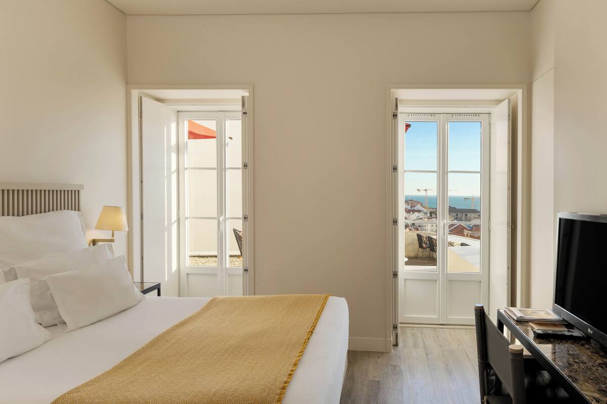 A hotel room with a bed, a TV, and a balcony with a view of the city.