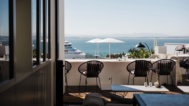 A terrace with outdoor seating, a view of the sea, and yachts in the background. - Memmo Alfama - Design Hotels (Lisbon)