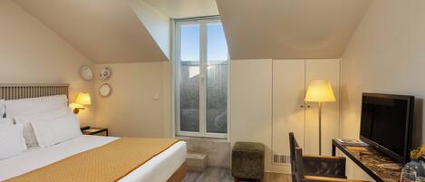 Habitación de hotel con cama, escritorio con televisor, un taburete pequeño y ventana con vistas.