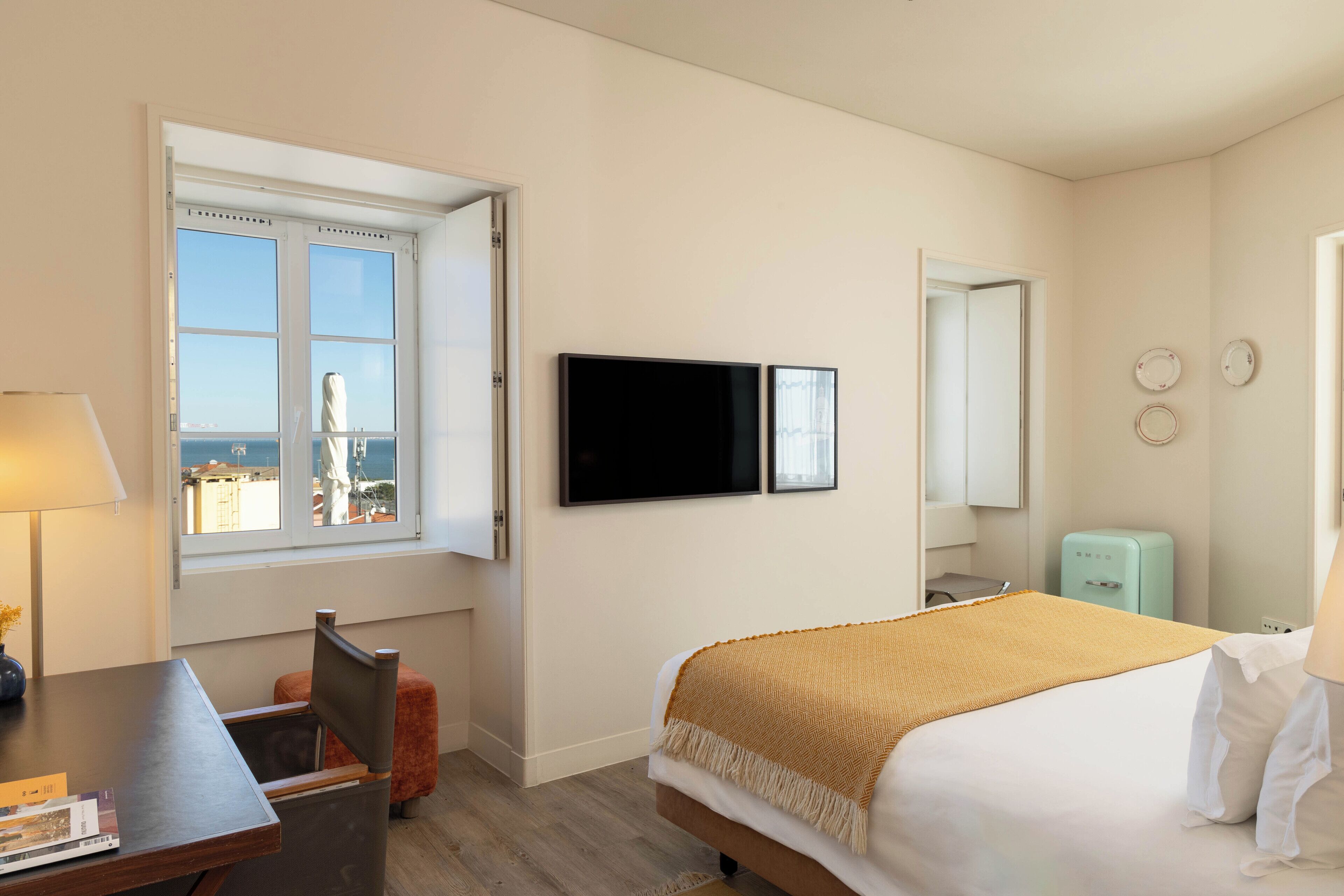 A hotel room with a bed, a desk, a chair, a television, a window with a view, and a small refrigerator.