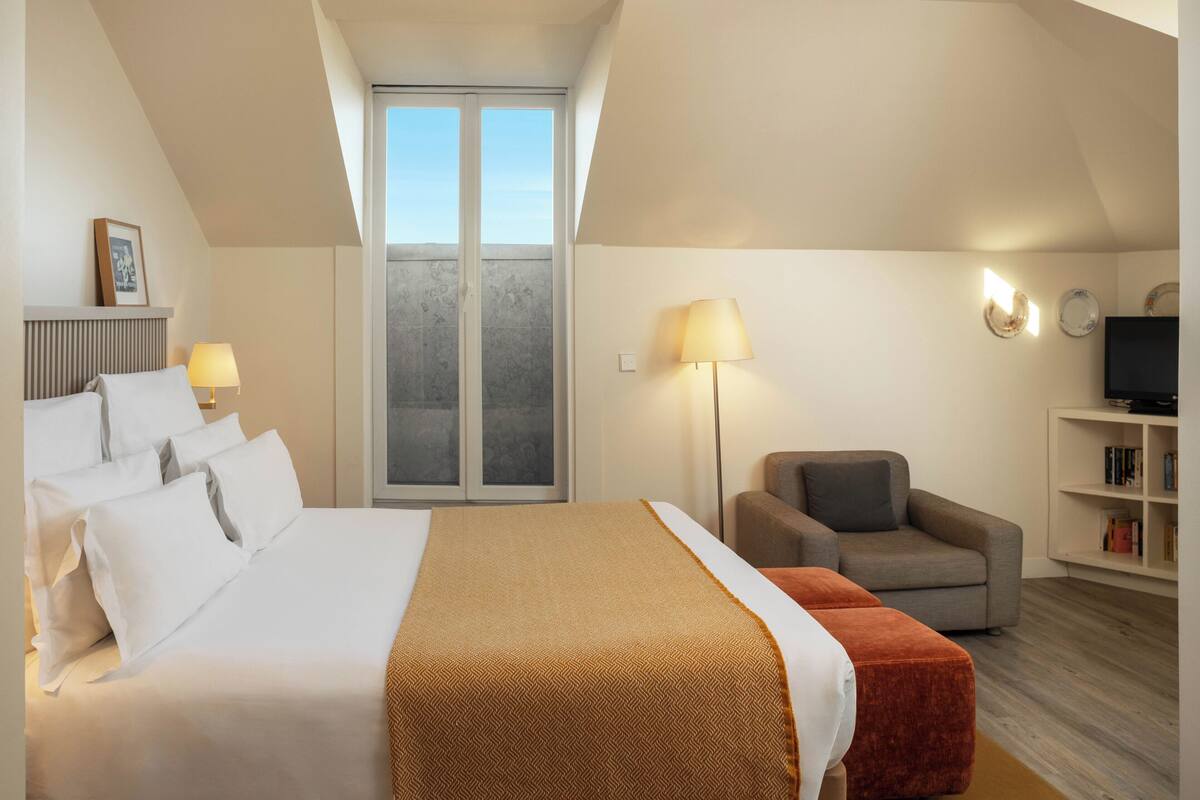 A hotel room with a bed, a sofa, a television, and a bookshelf.