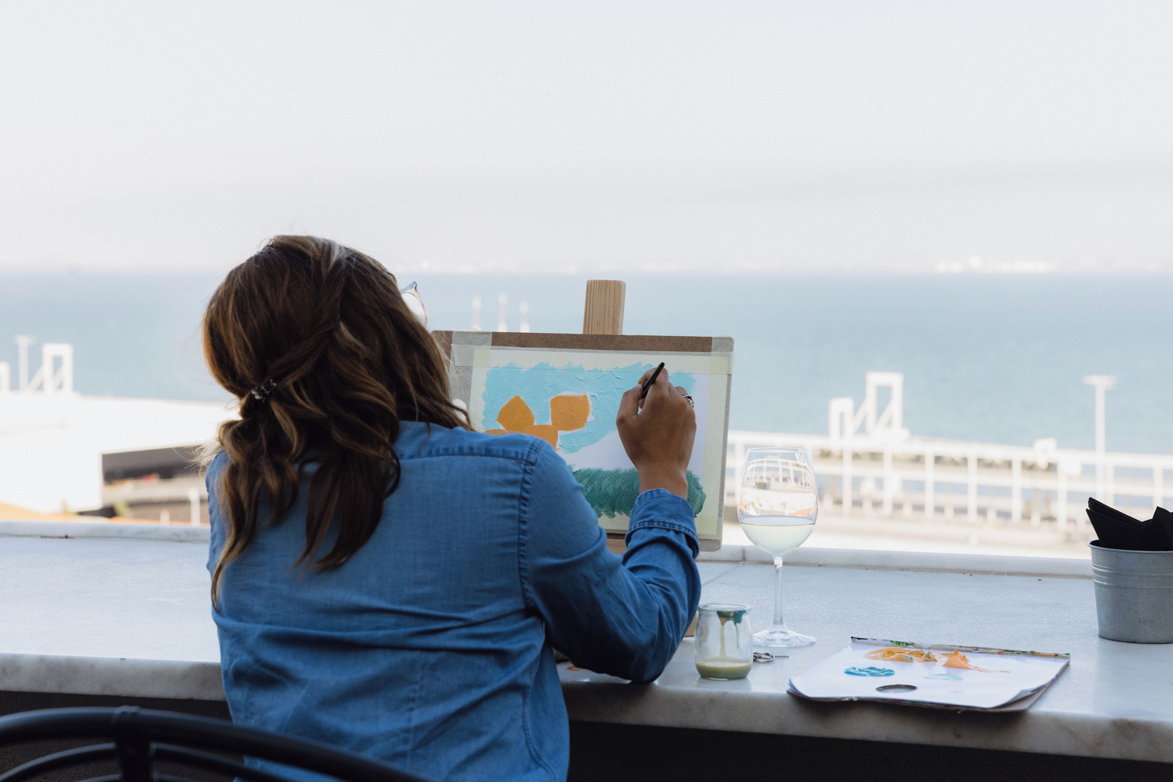 A person painting at a window overlooking the sea.