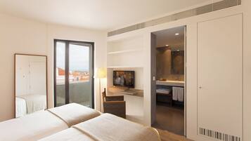 Habitación de hotel con dos camas, televisor, baño con espejo y vista a edificios.