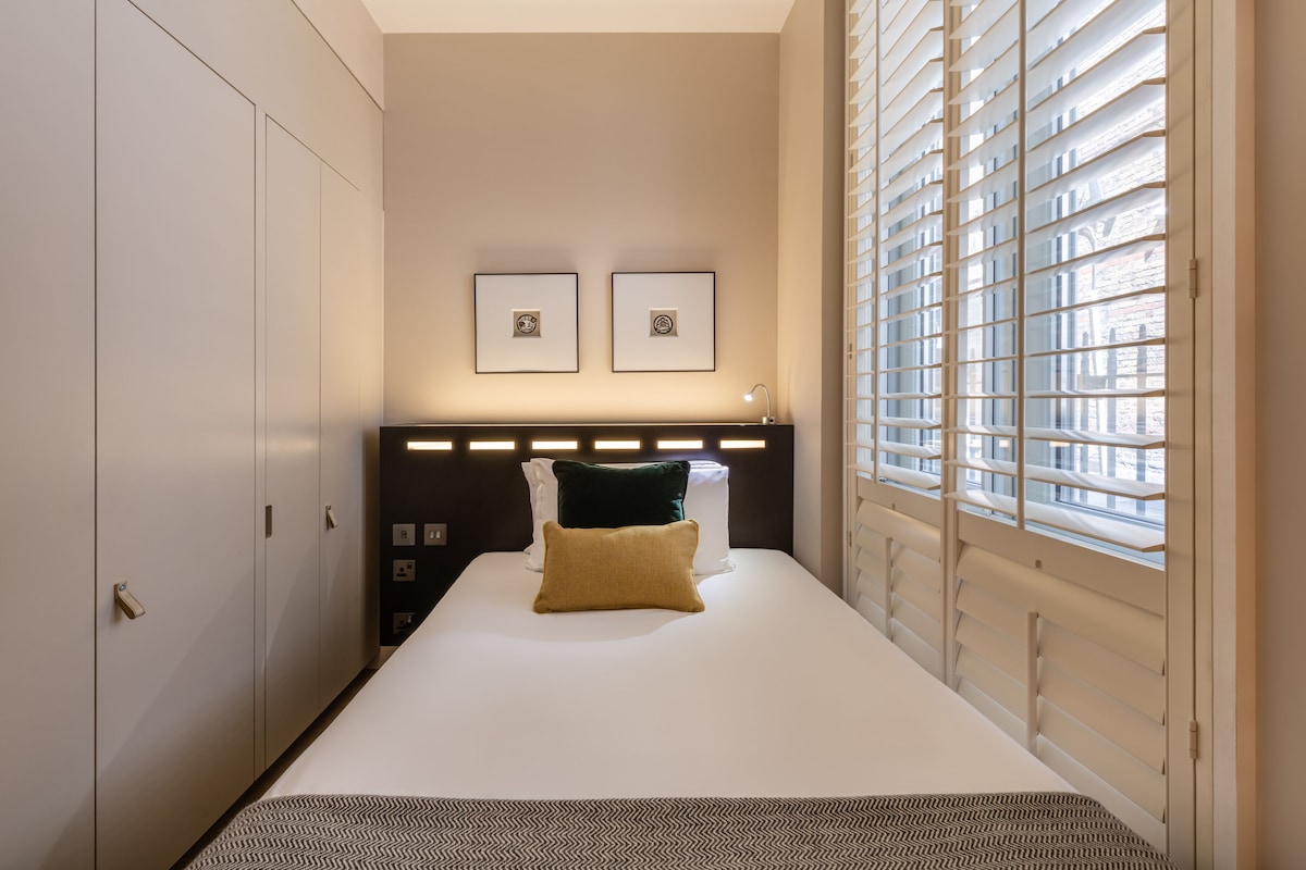 Quarto de hotel bem arrumado, com uma cama, um guarda-roupa e janela com persianas.