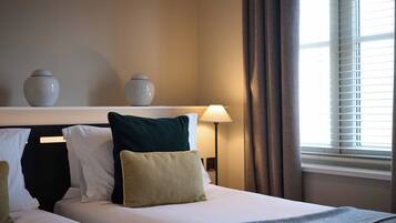 Ein Hotelzimmer mit Bett, Kissen, einer Lampe und einem Fenster mit Jalousien.