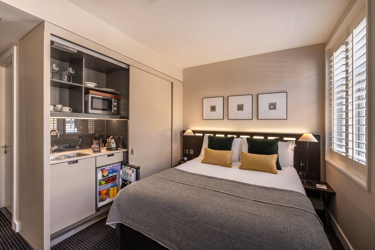 A hotel room with a bed, a minibar, a microwave, and a small kitchen area.