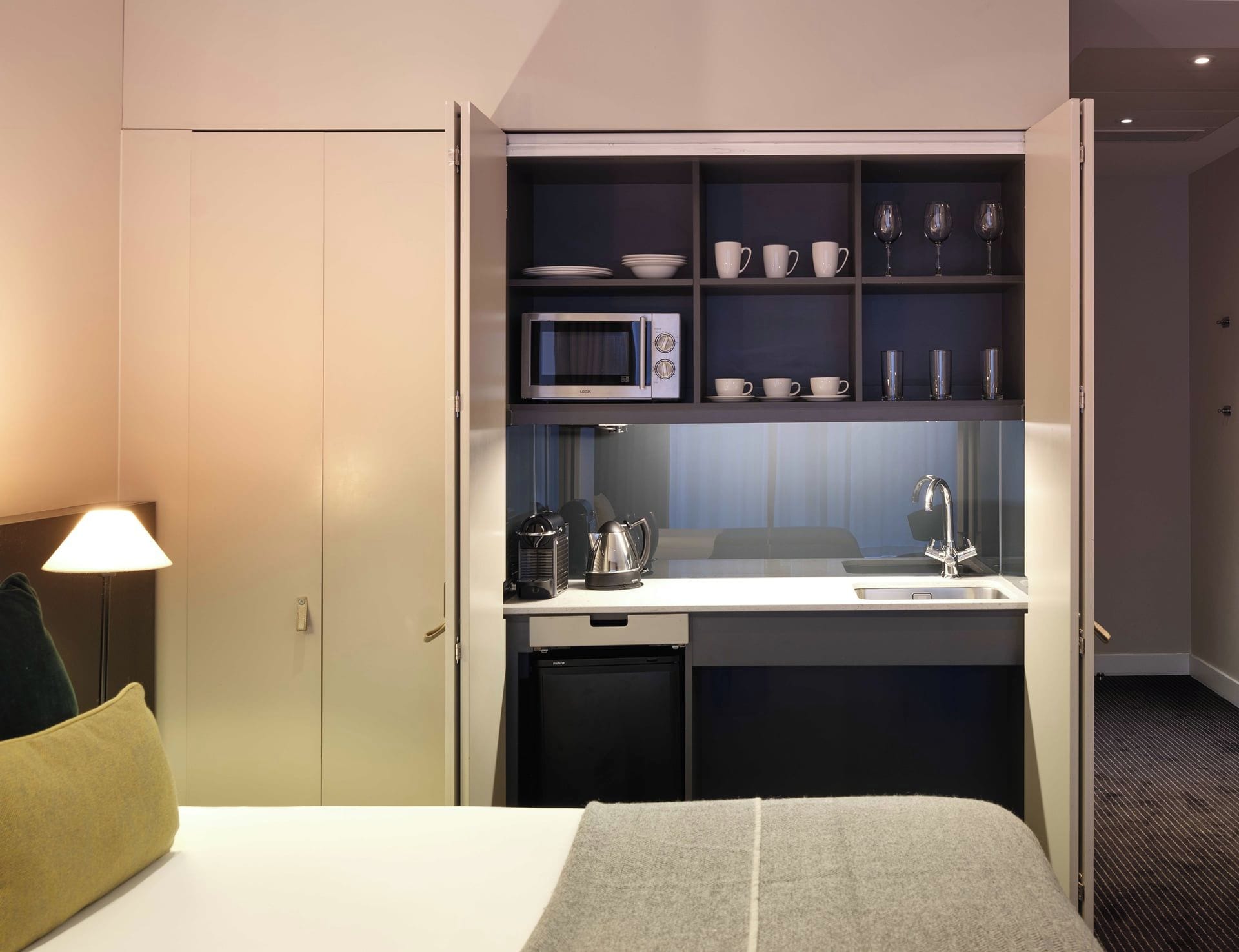 Habitación de hotel compacta con kitchenette, microondas, cafetera y lavabo.