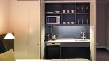 Habitación de hotel compacta con kitchenette, microondas, cafetera y lavabo.