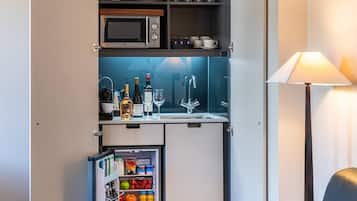A compact kitchenette with a microwave, wine bottles, and a mini-fridge stocked with fruits and beverages.