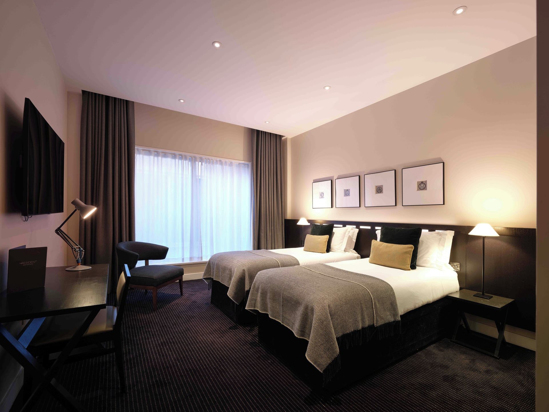 Een hotelkamer met twee bedden, een bureau, een stoel, een televisie en een raam met gordijnen.