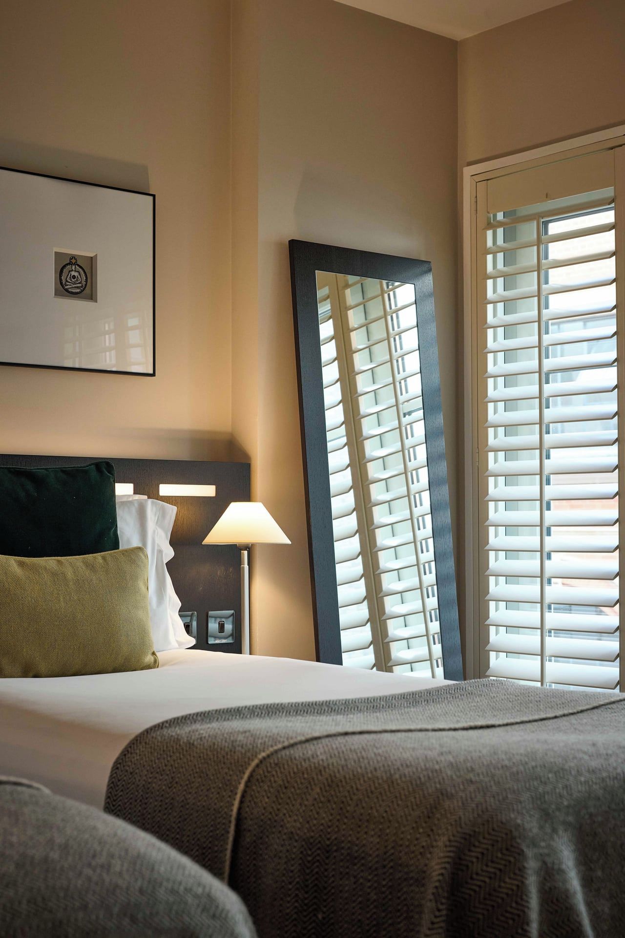 A hotel room with a bed, a nightstand, a lamp, and a window with blinds.