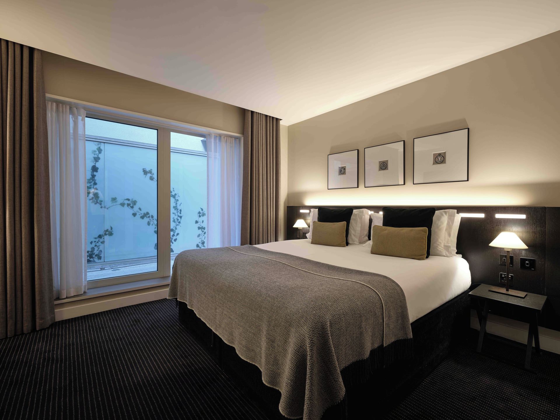 Una habitación de hotel con una cama grande, una mesita de noche, una lámpara y una ventana con cortinas.