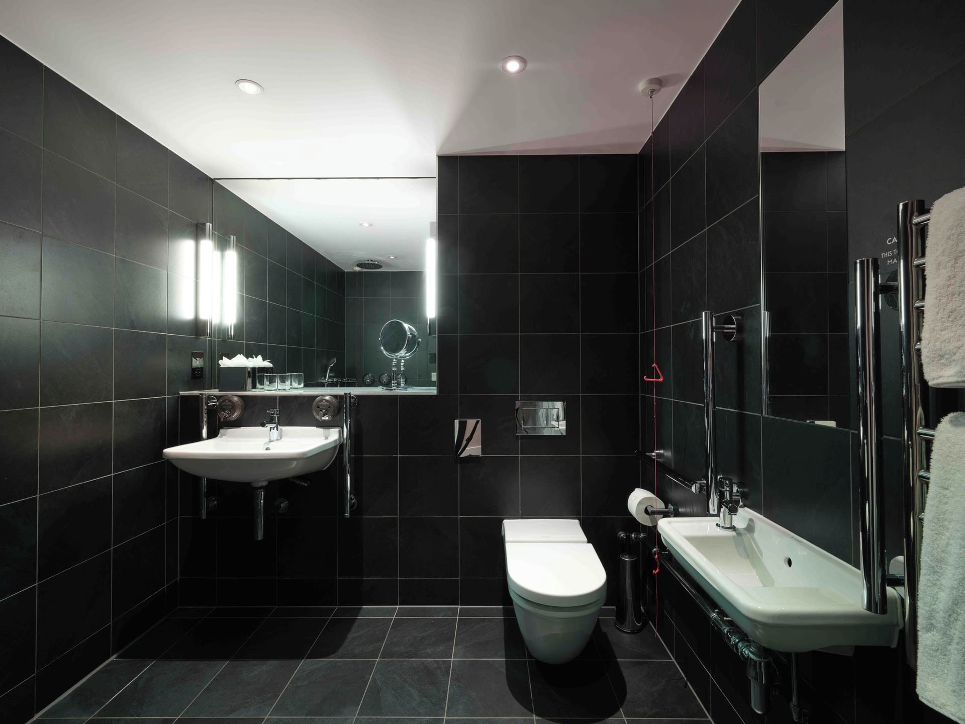 Een moderne badkamer met donkere tegels, een wit wastafelmeubel, toilet en douchehoek.