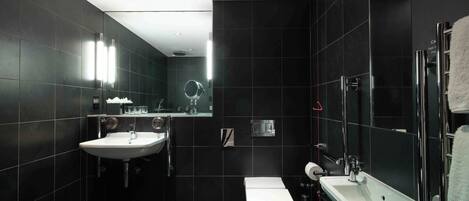 A modern bathroom with dark tiles, a white sink, a toilet, and a shower area.