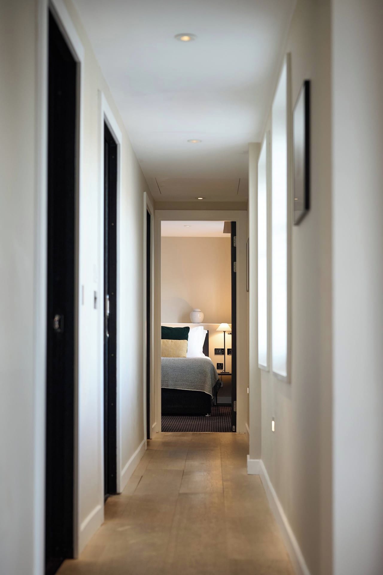 A hallway leading to a bedroom with a bed, bedside table, lamp, and a nightstand.
