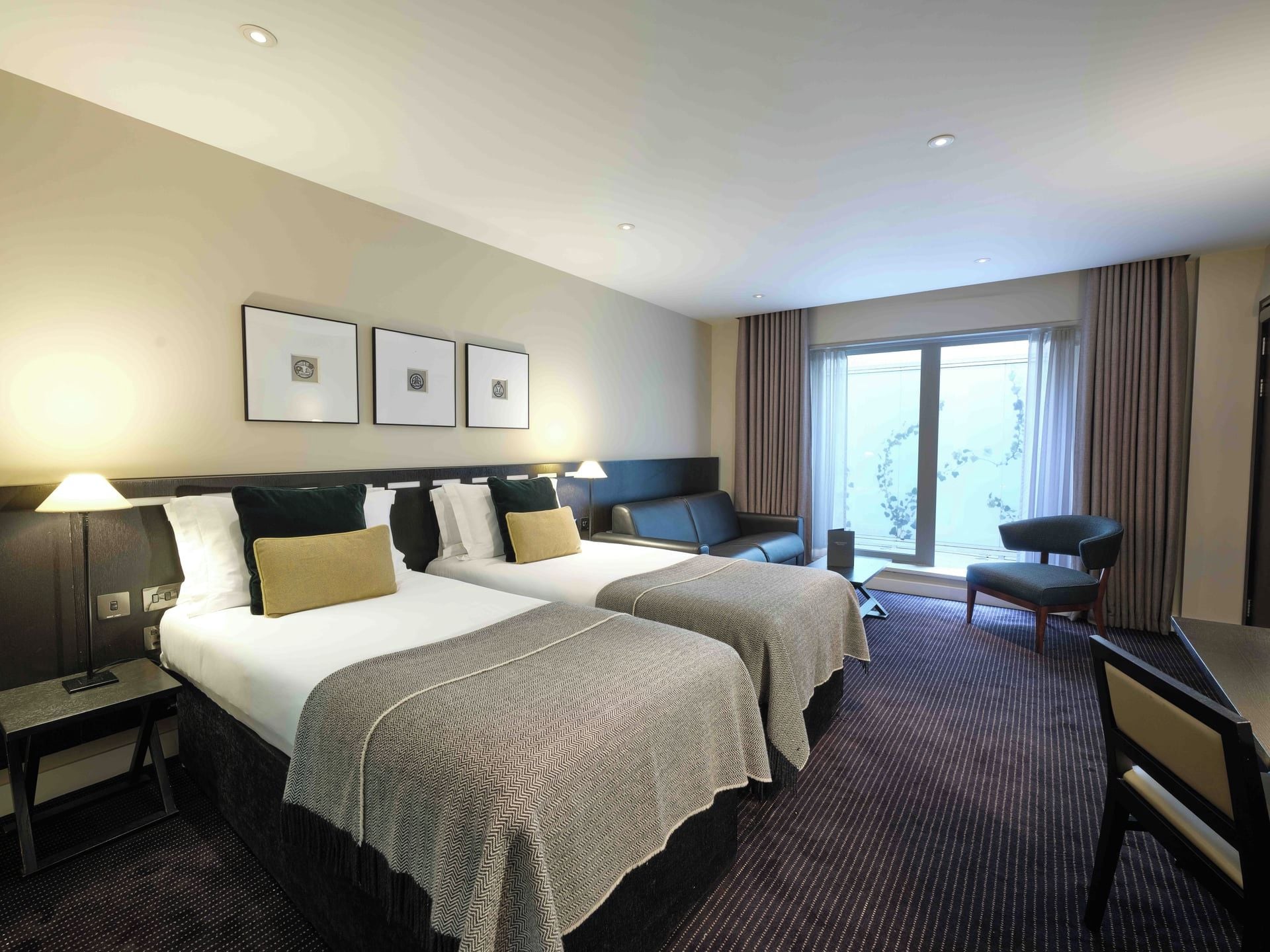 Een hotelkamer met twee bedden, een bureau, een stoel en een groot raam.