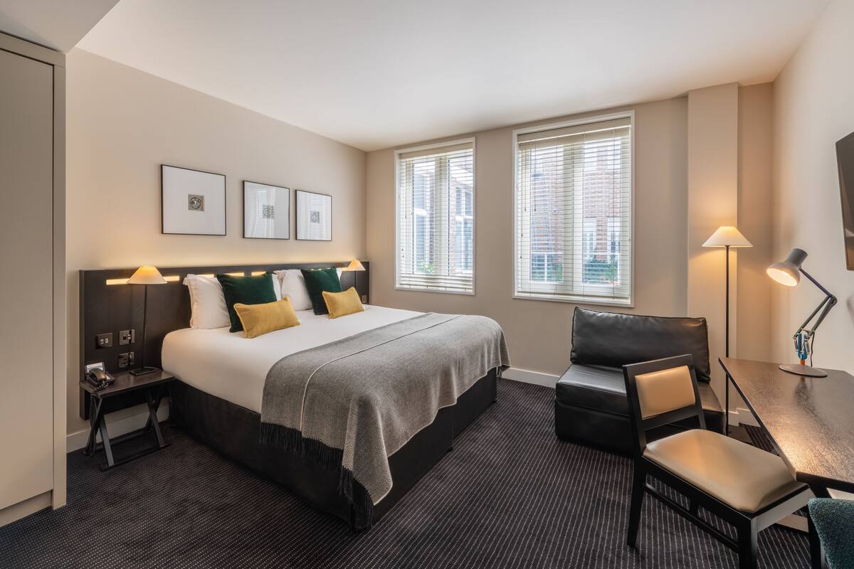 A hotel room with a bed, a desk, a chair, and a window with blinds.