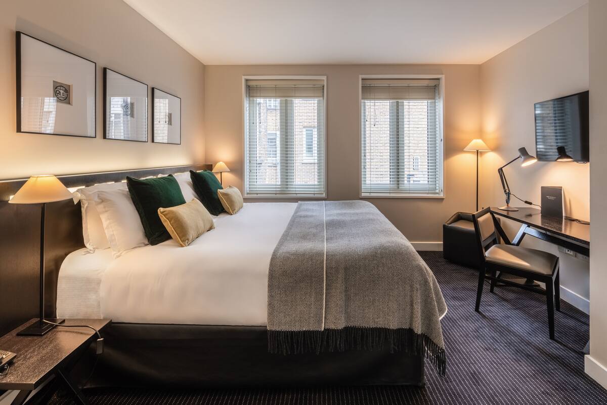 A hotel room with a large bed, two bedside lamps, a desk with a chair, and a television on the wall.