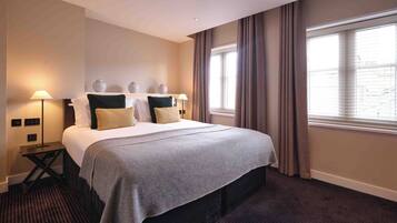 A hotel room with a bed, bedside lamps, a nightstand, and a window with curtains.