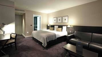 Quarto de hotel com cama, escrivaninha, cadeira, sofá e mesa pequena.