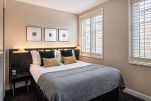 A hotel room with a bed, bedside lamps, a nightstand, and a window with blinds. - The Resident Soho (London)
