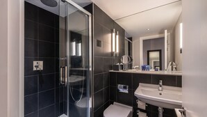 A modern bathroom with a glass-enclosed shower, a white toilet, and a sink with a mirror above it. - The Resident Soho (London)