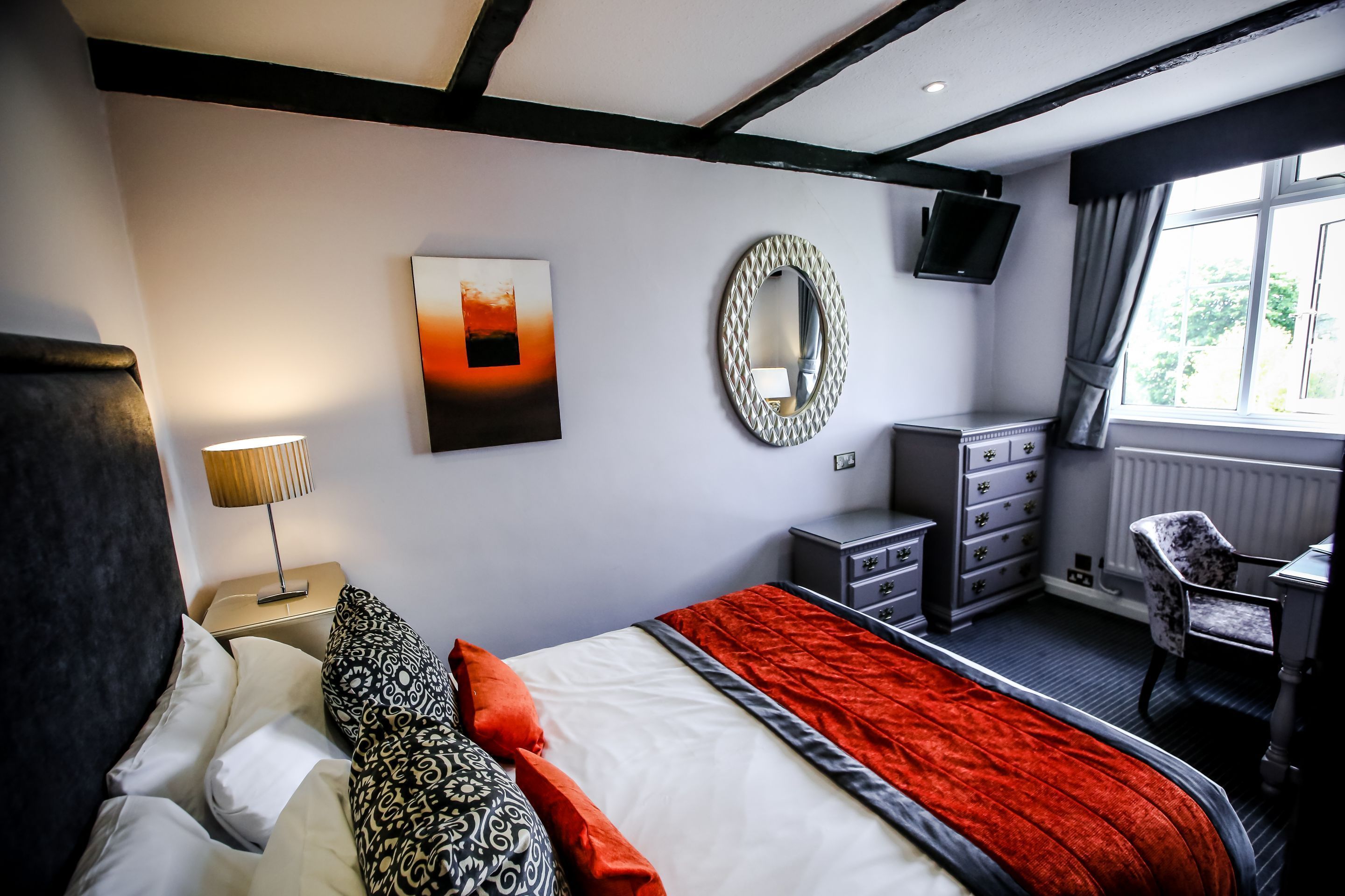 Una habitación de hotel moderna con una cama grande, un escritorio, una silla, un televisor y una ventana con cortinas.