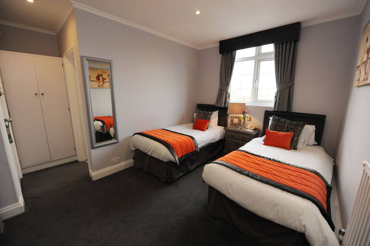 A hotel room with two beds, a wardrobe, a mirror, and a window with curtains.