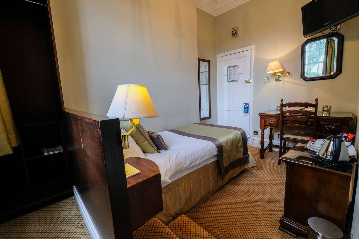 A hotel room with a bed, a desk, a chair, a lamp, a dresser, and a television.
