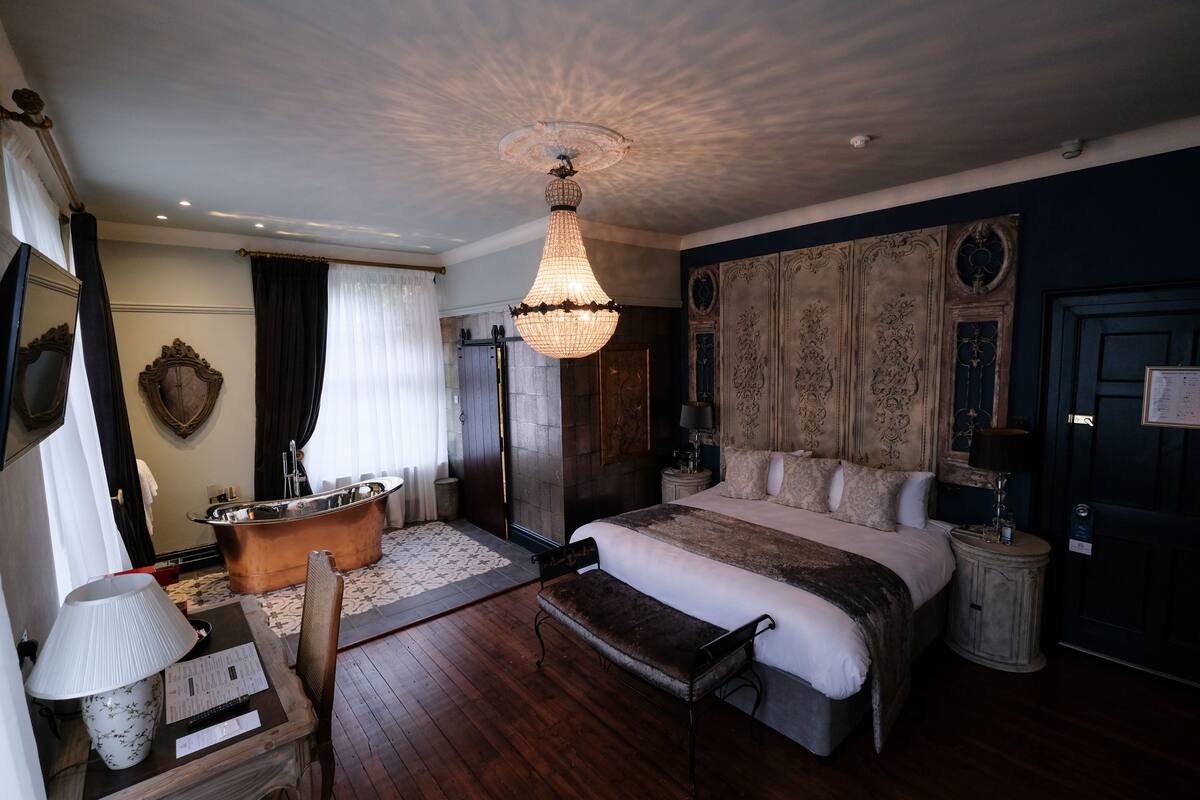 A bedroom with a large bed, a wooden bench, a bathtub, and a chandelier.