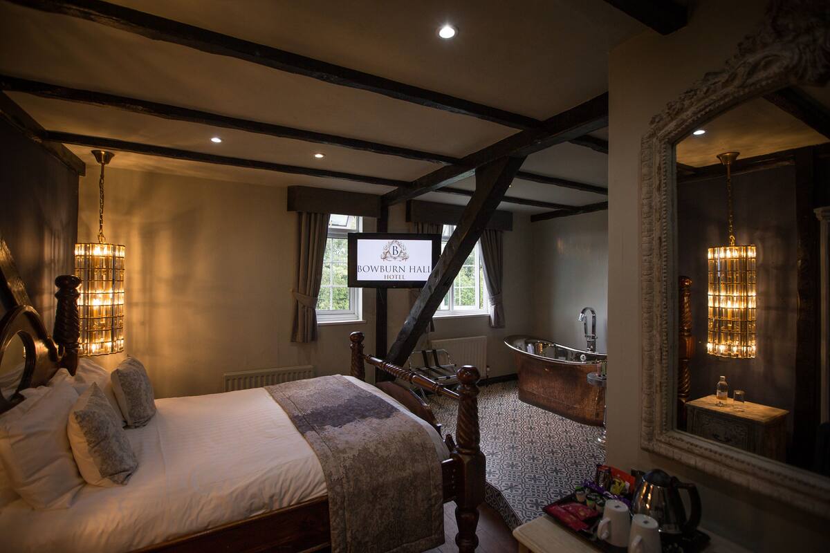A hotel room with a large bed, a sitting area with a view, a television, and a bathroom with a bathtub.