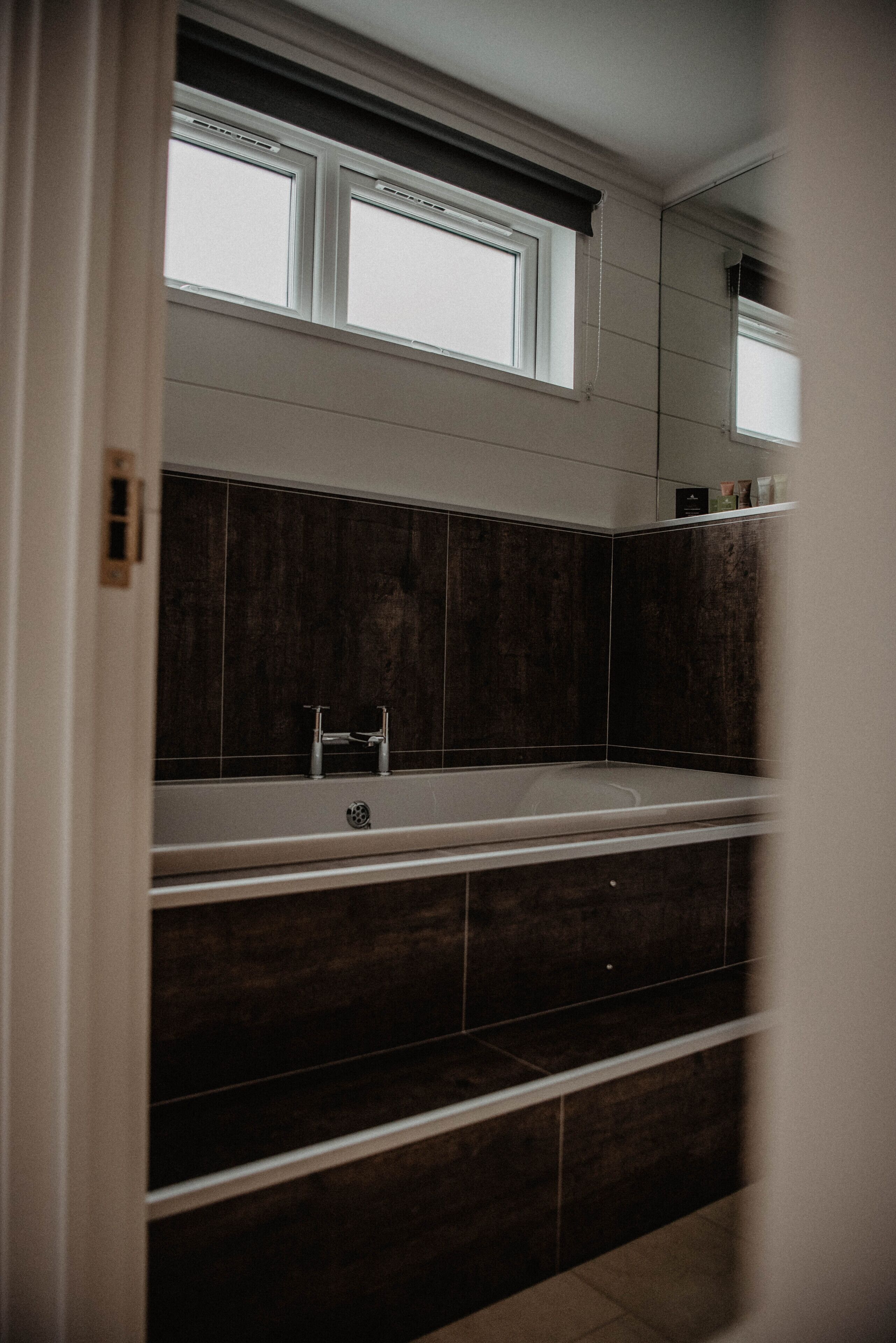 Un baño moderno con una bañera grande, baldosas oscuras y una ventana sobre el lavabo.
