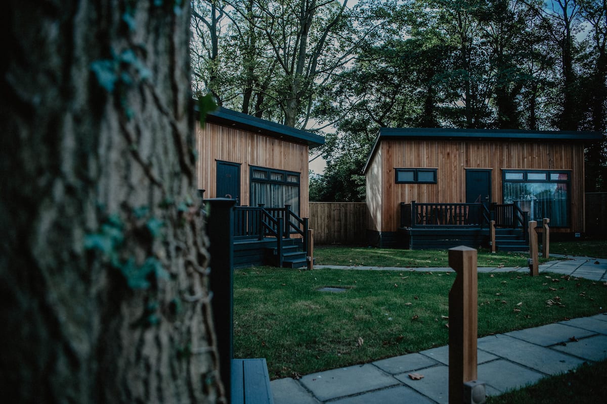 Two wooden cabins with external stairs, surrounded by a grassy area and trees.