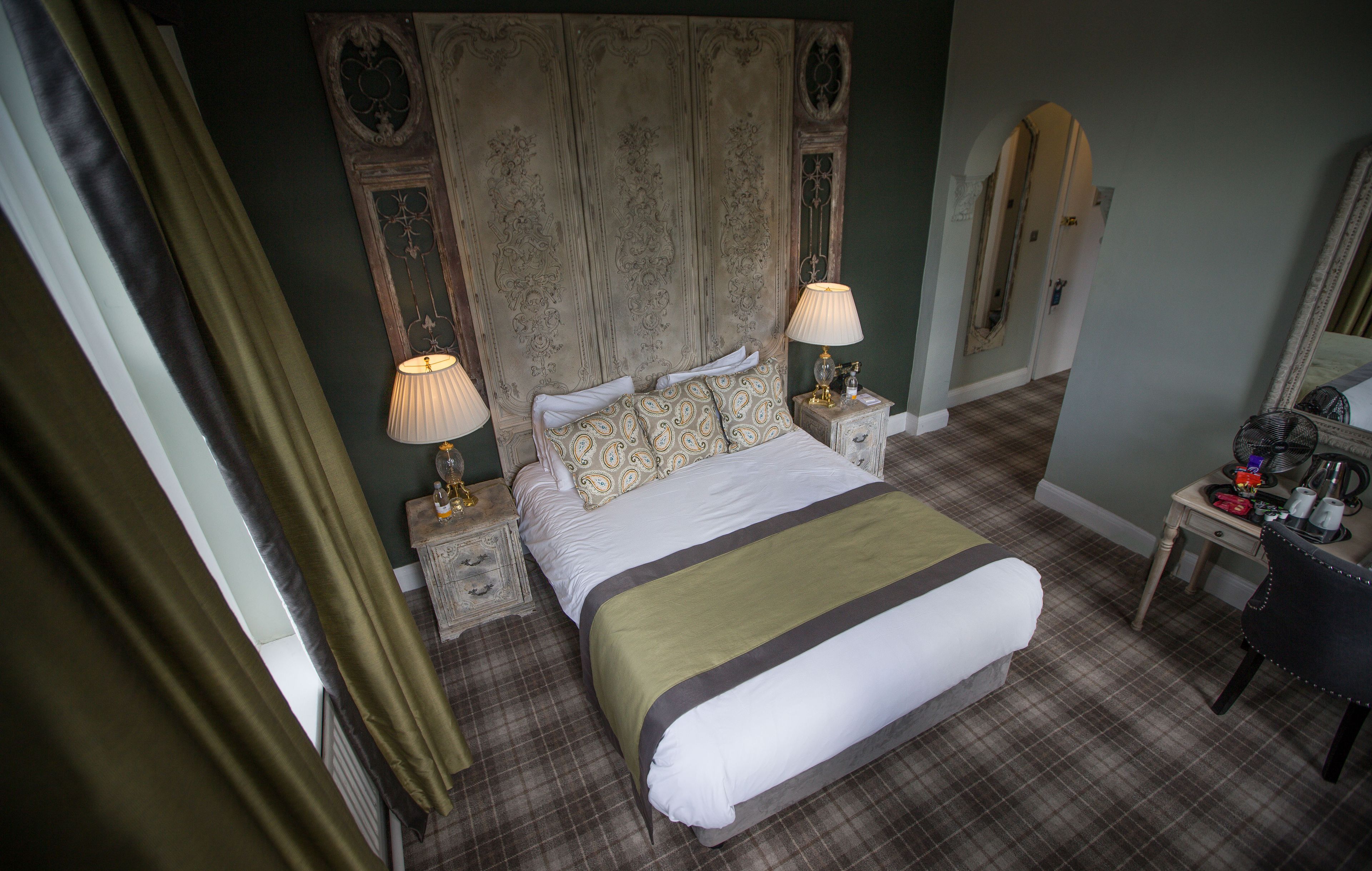 A hotel room with a large bed, two bedside tables with lamps, a chair, a desk with a mirror, and a wardrobe.